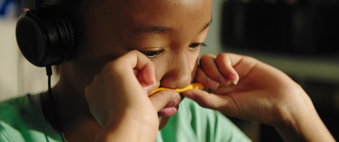 A girl with a headphones putting a pencil up to her nose