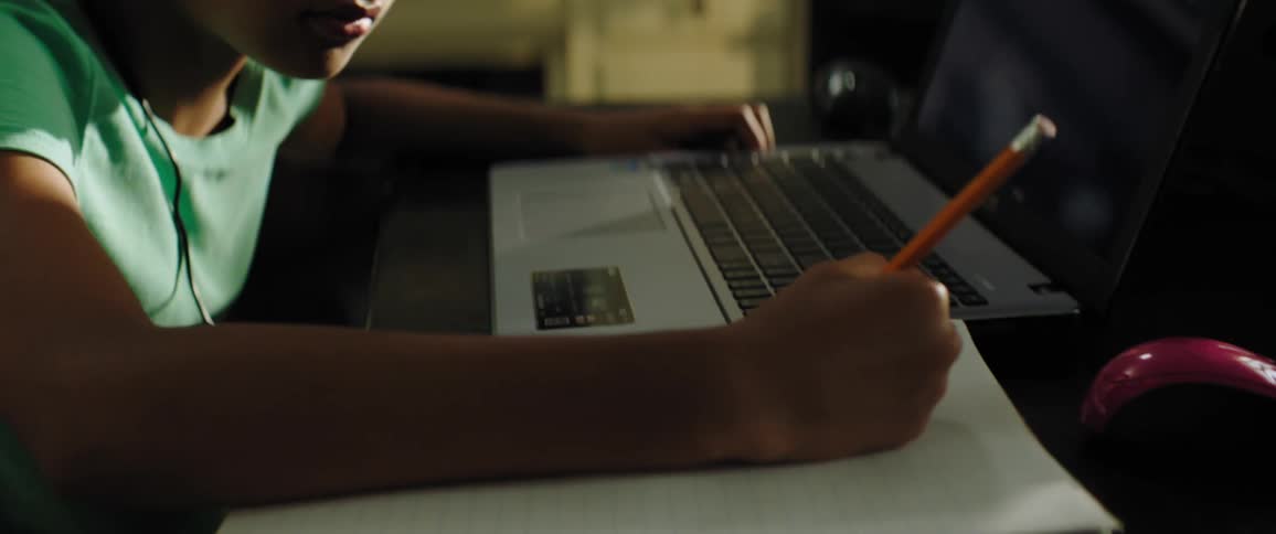 Black girl with a turquoise shirt and black headphones sits at the table and writes in a notebook