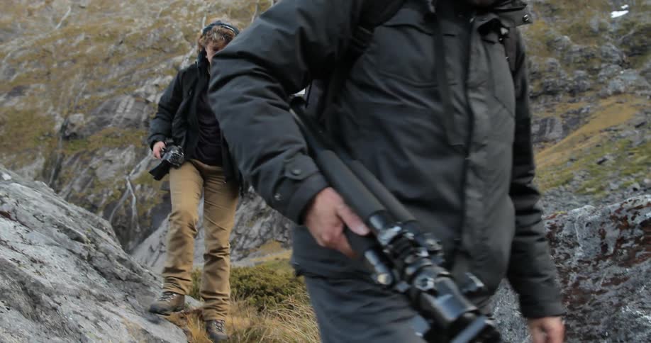 Man and woman carry camera equipment over rocky terrain