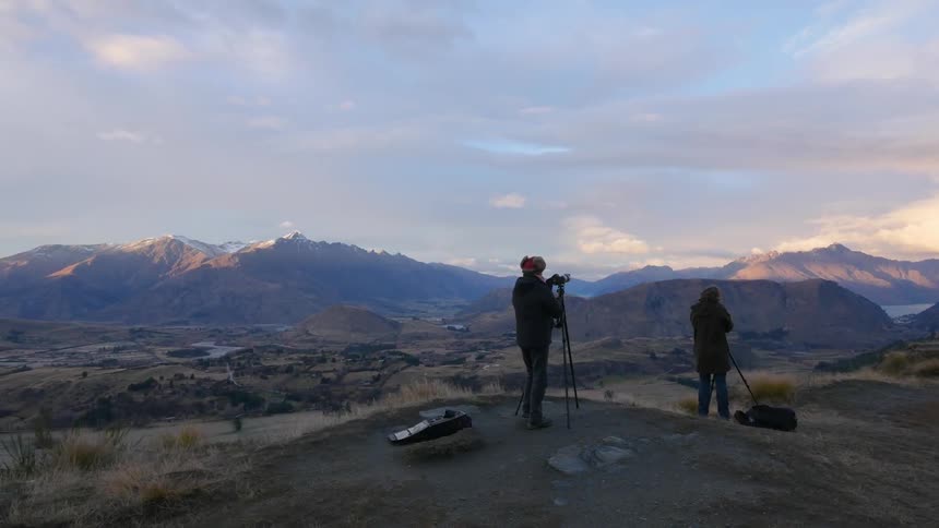 A couple adjust their cameras on a hill at sunset