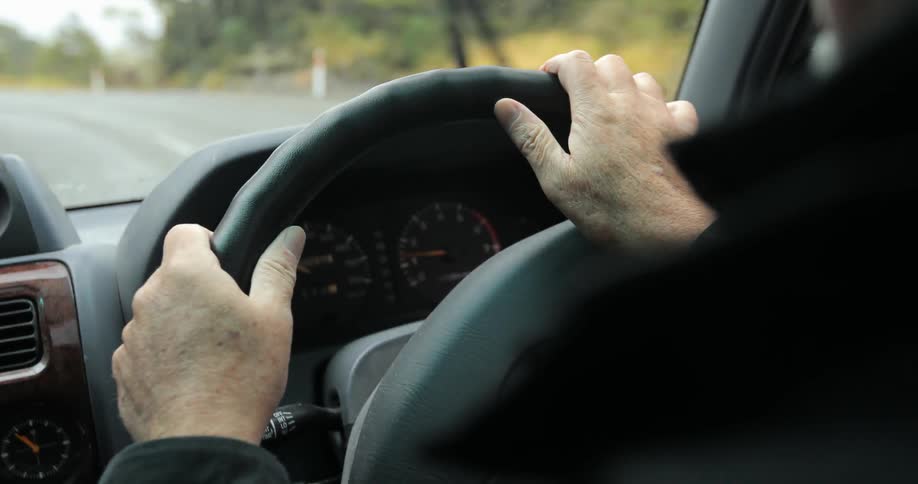 Close-up of a person steering a vehicle as seen from the rear seat