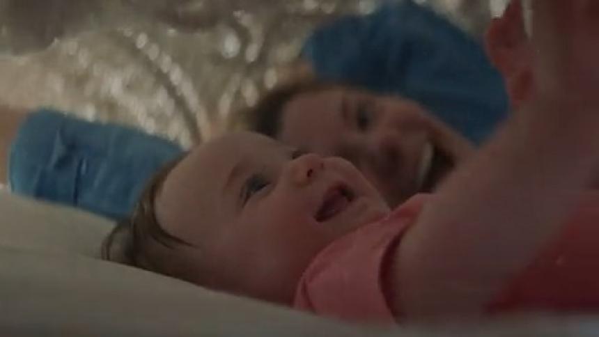 A mother uses a blanket to play with her baby on a bed