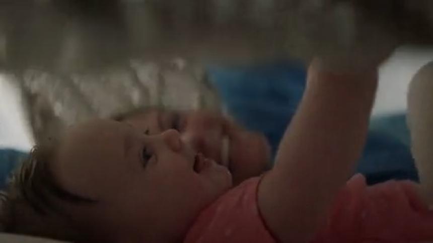 A mother and daughter laying together on a bed as the mother covers them in a blanket