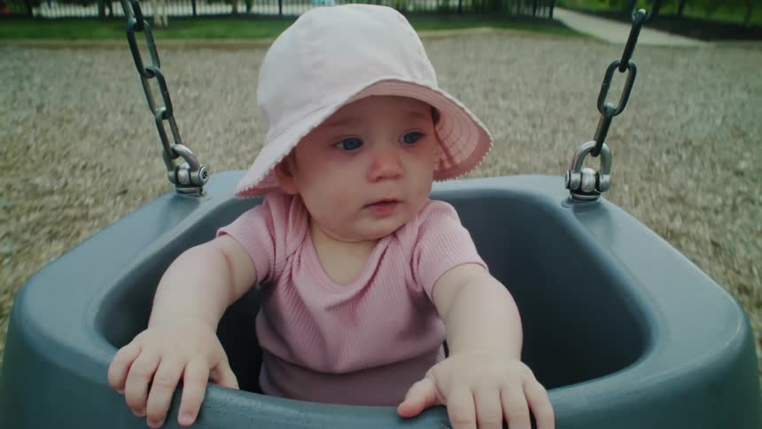 A baby sitting in a swing as it swings back and forth and the baby rocks with it