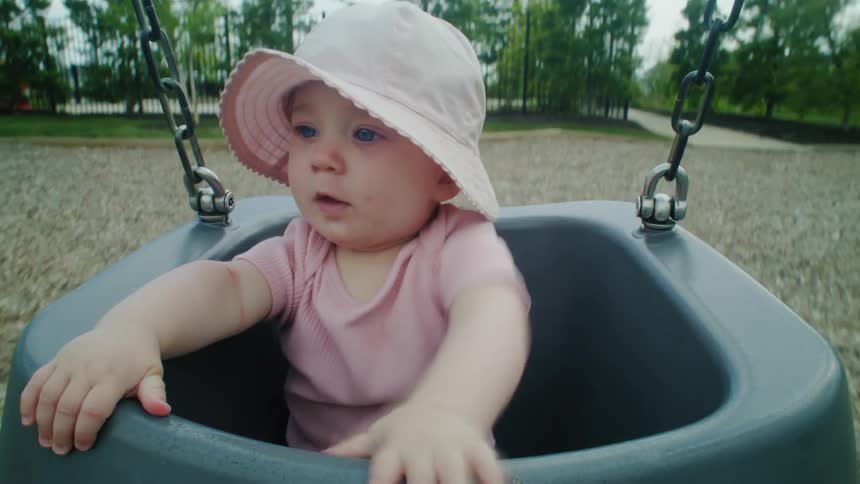A young baby wearing hat enjoys swinging in a park swing