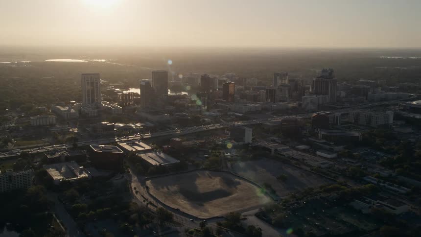 Aerial footage orbiting Downtown Orlando at sunrise showing the metropolis bathed in sunshine and the glowing sun in the distance over Floridas East Coast