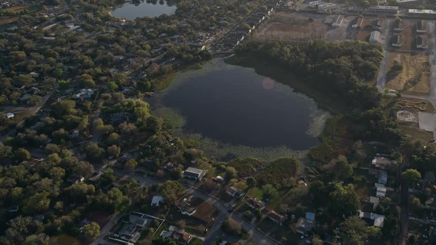 Aerial approach at sunrise to Druid Lake in Orlando Florida showcasing the sunny shoreline and nature surrounding the water body