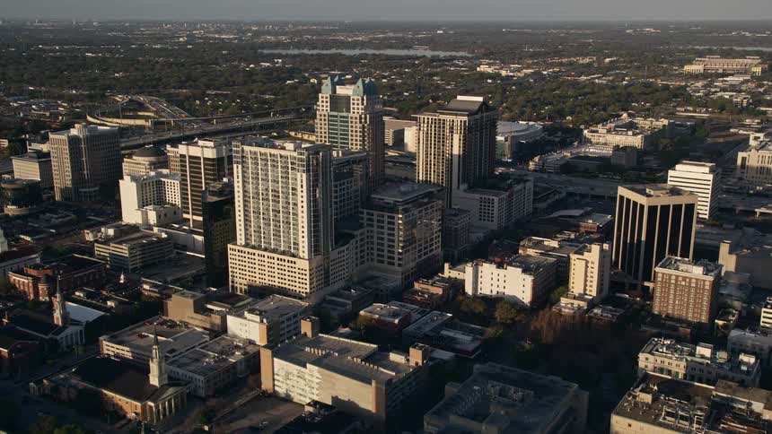Approach office buildings and arena in downtown Orlando at sunrise as seen from aerial view flying over Lake Eola