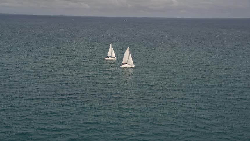Two catamarans reveal and orbit near South Beach Florida with a tilt up from calm ocean waters