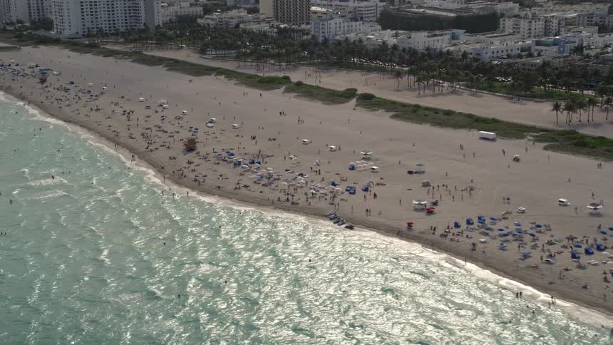 Aerial footage of people enjoying the beach by condos in South Beach Florida with a downward tilt