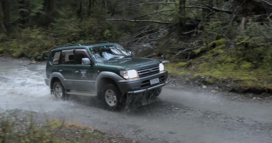 A vehicle splashes through the water on a trail