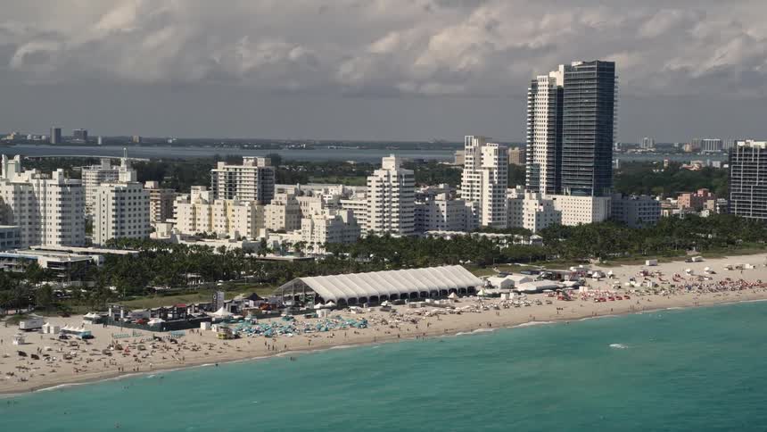 View of a crowded Miami Beach shoreline with beachgoers and hotels visible from aerial 5K footage