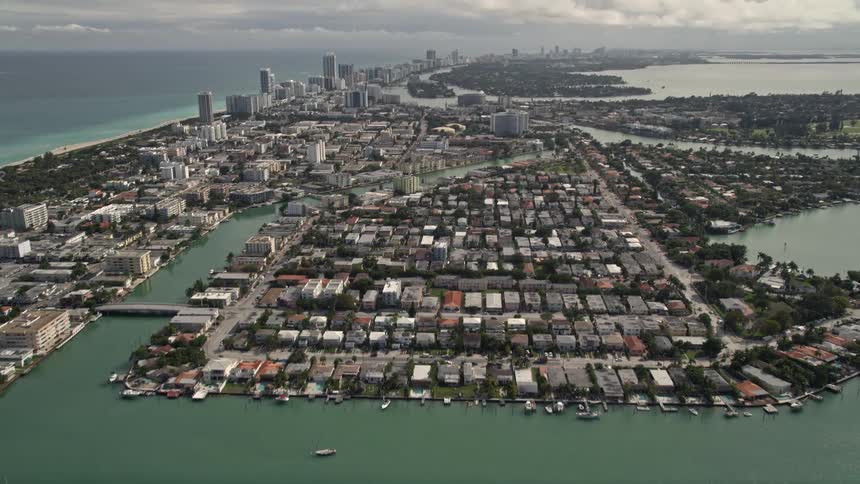 An aerial shot of Surfside neighborhoods in Miami Florida tilts up to reveal Biscayne Point and Miami Beach amidst partly cloudy skies