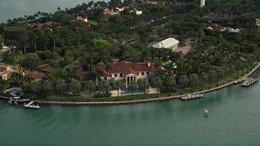 An aerial view of a grand mansion on the bayfront of Star Island Florida surrounded by upscale homes and docks into the water