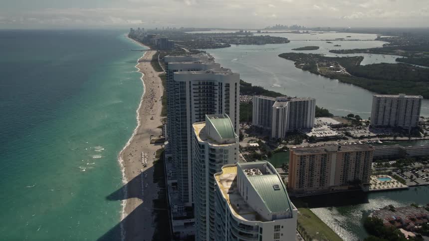 A stunning aerial view of the beach and pier oceanfront hotel and high-rises in Sunny Isles Beach Florida with people enjoying recreation and relaxation on the shores