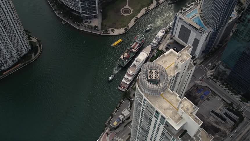 A stunning aerial fly over showing several boats passing through a water passageway surrounded by multiple skyscrapers including the Southeast Financial Center and residences approaching in Downtown Miami Florida