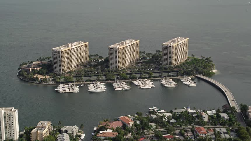 An aerial view of three condominium complexes on Grove Isle in Miami Florida with boats docked at the pier and a bridge connecting it to the mainland