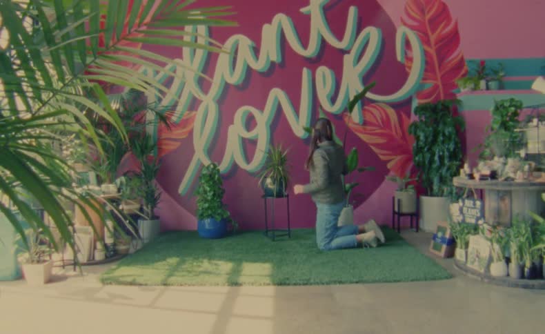 Mother wearing jacket trims plant while kneeling in plant store