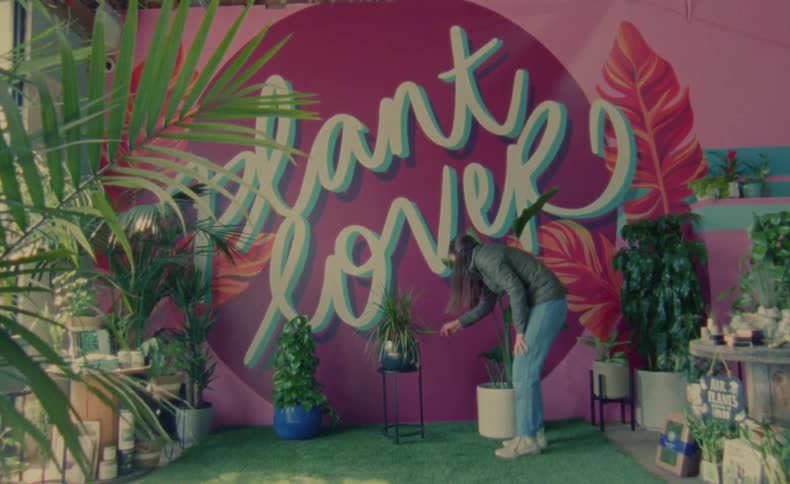Woman places potted plant on stand near mural in plant store