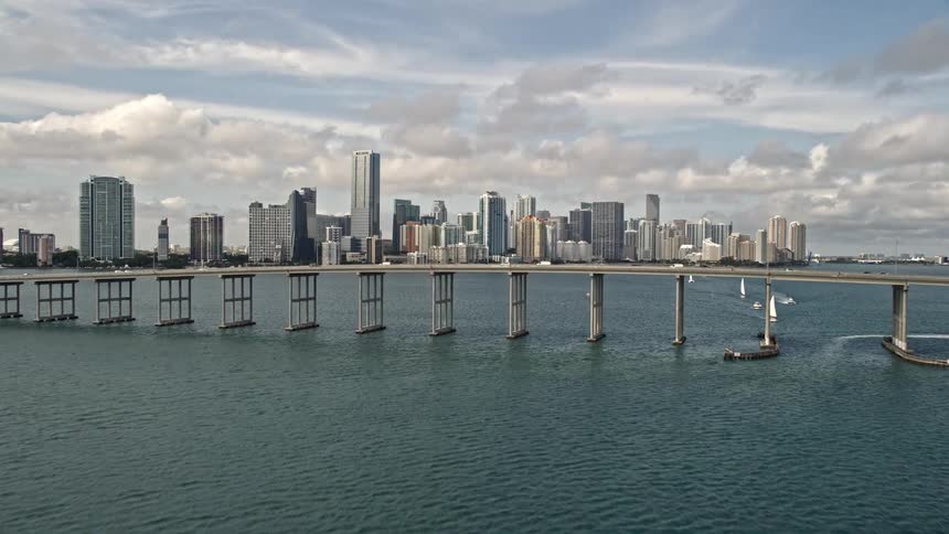 Approaching and revealing the Rickenbacker Causeway and Downtown Miami skyline while flying over the coastline of Florida in a low altitude aerial footage