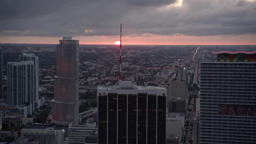 A stunning aerial shot revealing Downtown Miamis tall skyscrapers bathed in the setting suns glow against a cloudy skyline - an iconic Miami scene and perfect for footage of South Florida and Miami