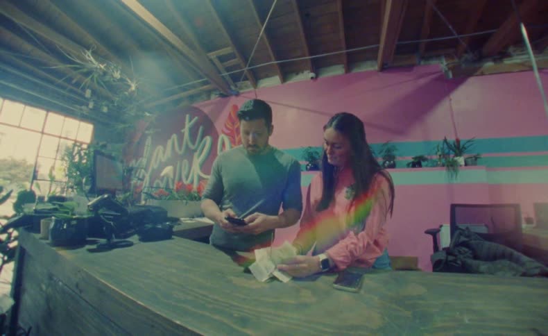 A man and woman standing next to each other at a store counter while looking at receipts and typing on their phones