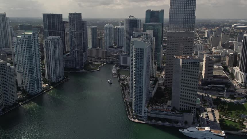 Aerial view of fishing boats in the bay tilting up to reveal downtown Miamis skyscrapers and river with a coastline and nature in the foreground
