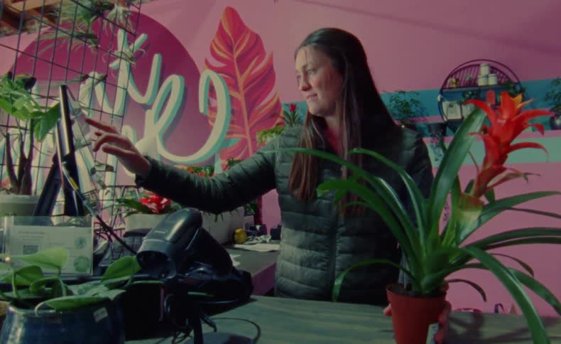 A woman standing behind a checkout counter scanning a plant and typing on the computer