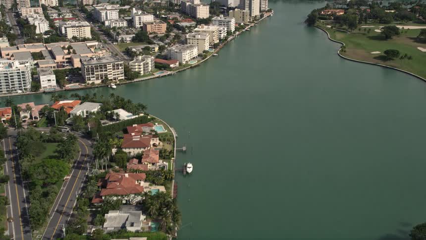 A stunning aerial of waterfront houses with boats docked in a coastal community on Bay Harbor Islands Florida tilting up towards the city skyline