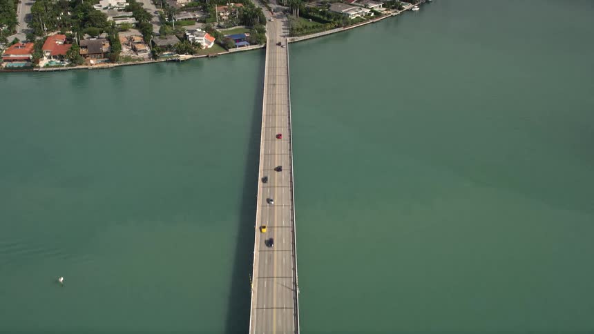 A birds eye view of light traffic on Broad Causeway tilting up to reveal Bay Harbor Islands neighborhoods offering a beautiful glimpse of the Florida coastline