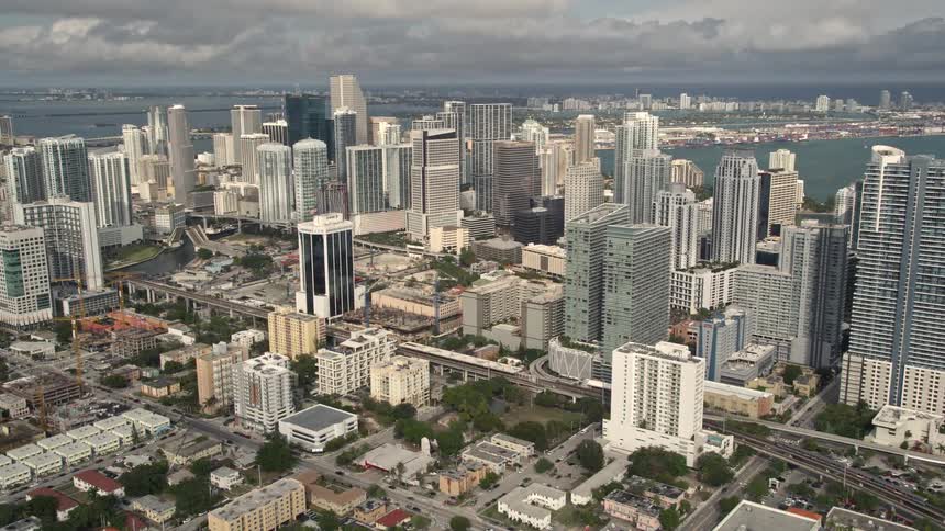 Aerial footage captures the towering skyscrapers of Downtown Miami Florida during the day with partly cloudy skies and a side view perspective
