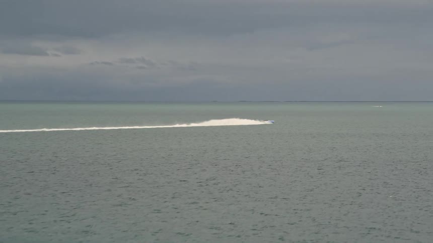A sport boat races on Biscayne Bay leaving a trail of splashes behind it as seen from an aerial view