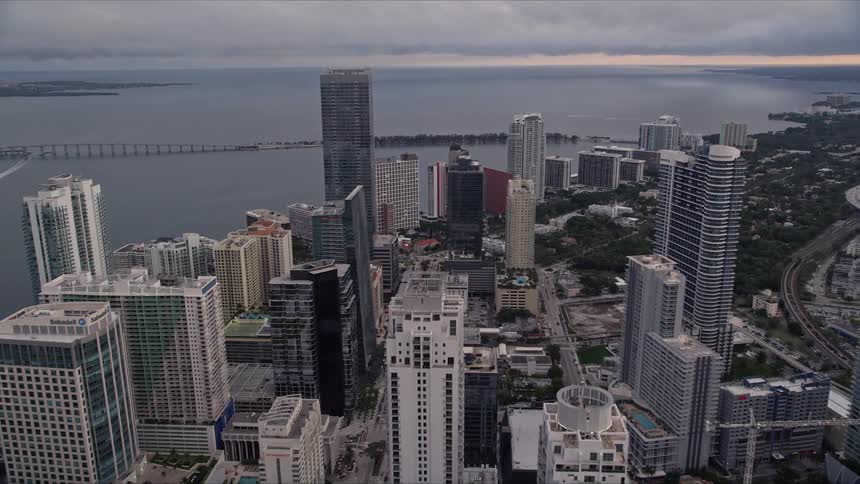 Fly over Downtown Miami skyscrapers at sunset towards Rickenbacker Causeway capturing a breathtaking view of Biscayne Bay