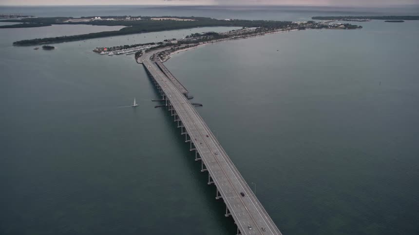 A stunning aerial shot at dusk of the Rickenbacker Causeway bridge connecting coastal land over Biscayne Bay at sunset in southern Florida