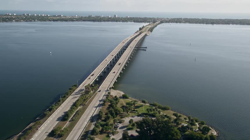 A sunny day-time aerial view of the Melbourne Causeway bridge over the Indian River displaying light traffic and the beautiful nature of Floridas east coast