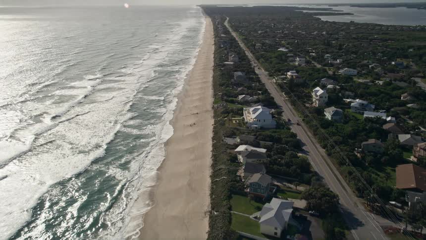 An aerial video clip of residential homes situated on a beach in Melbourne Beach Florida with a sunny and scenic environment visible as the camera approaches the shoreline and captures the beachfront property