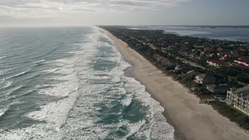 An aerial view of waves crashing against Melbourne Beach in Florida capturing the stunning coastline and numerous large residences lining the sandy shore