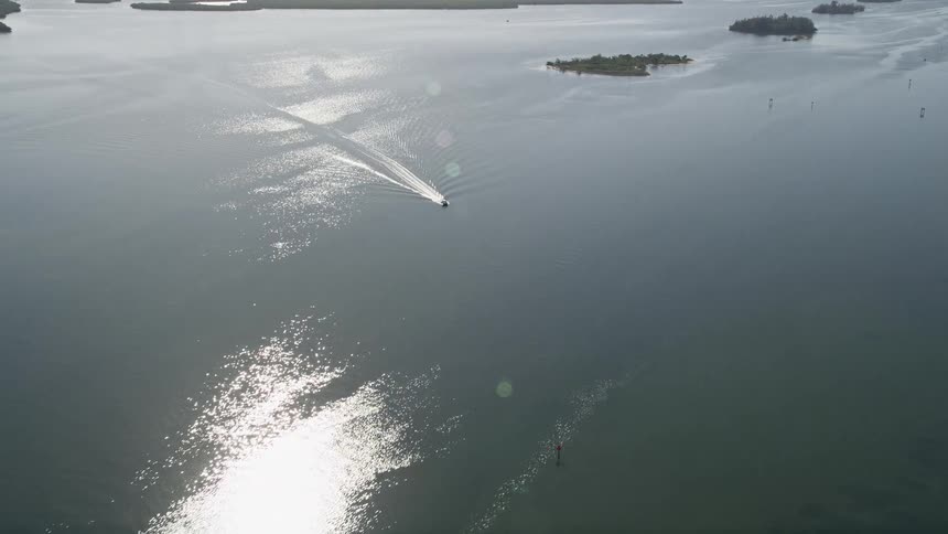 An aerial view of a fishing boat approaching and tracking through the Indian River in Florida on a sunny day