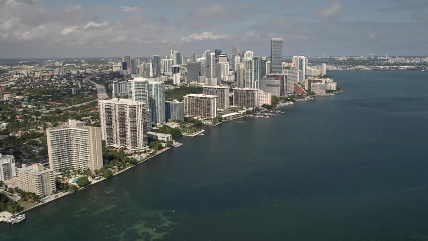 An aerial tilt up from Rickenbacker Causeway to reveal the residential high rises condos and supertalls of Downtown Miamis skyline along the shoreline of Biscayne Bay Florida