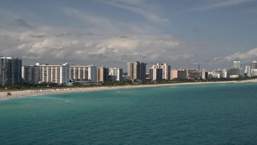 Aerial view of a row of condominiums along the beachfront in Miami Florida surrounded by a lively atmosphere of sunbathers and beachgoers enjoying a partly cloudy day