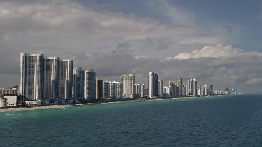 Aerial footage of oceanfront skyscrapers and buildings along the coast in Sunny Isles Beach Florida under cloudy skies