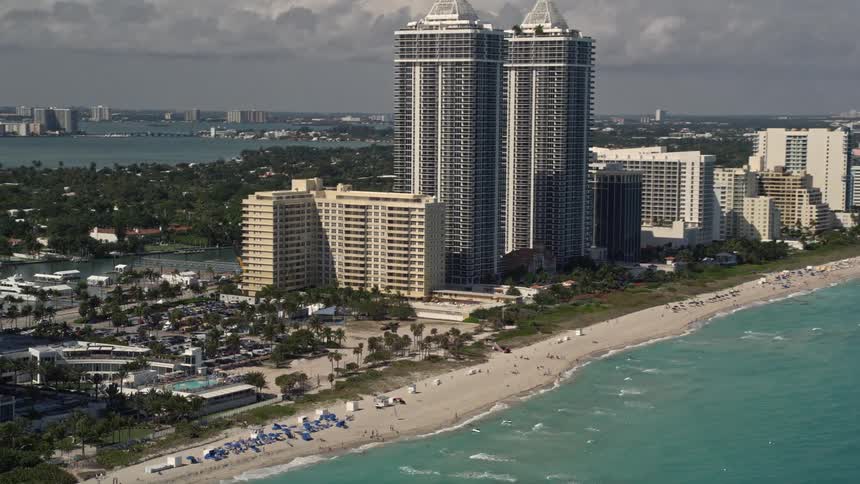 Aerial view of twin towers of Miami Beach skyscrapers with sunbathers and beachgoers enjoying the coastline and recreation on the shore