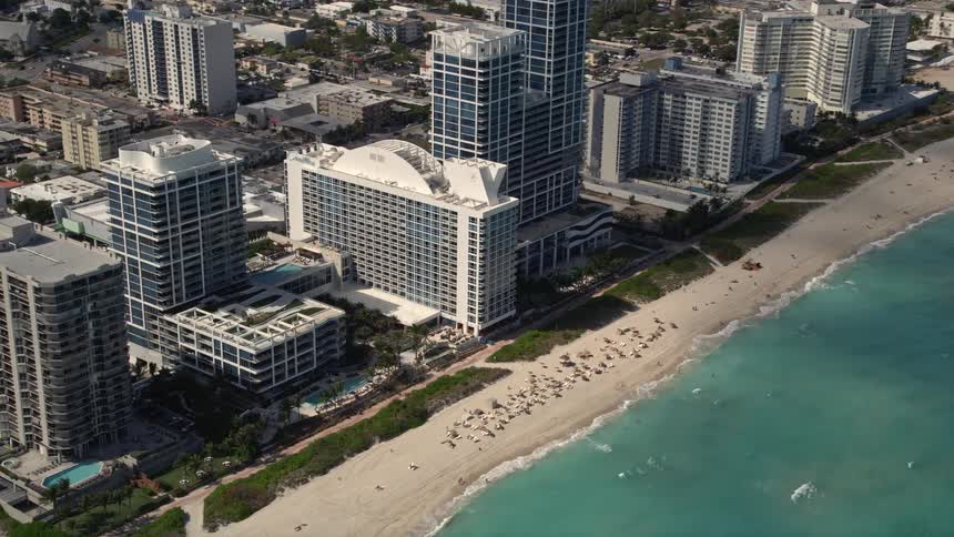 An aerial flyby of beachfront hotels with a tilt down to sunbathers enjoying the sunshine in Miami Beach
