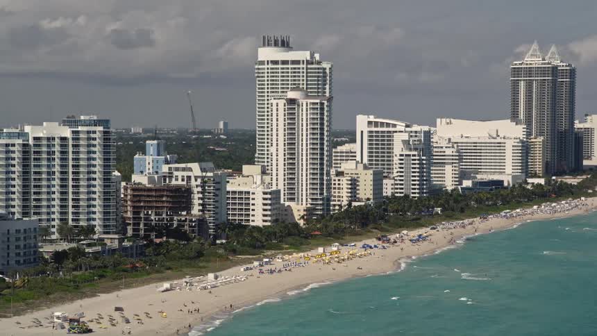 Approaching the Fontainebleau Miami Beach Hotel by aerial view with a crowded shoreline of sunbathers and beachgoers enjoying the southern Florida coast
