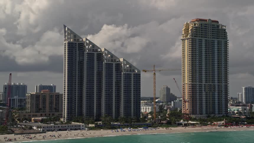 Aerial footage of an oceanfront city with high-rise condominium and resort hotel overlooking a cloudy beach