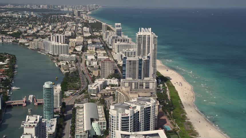 Aerial flyover of beachfront condos in Miami Beach with clear views of the shoreline and city skyscrapers