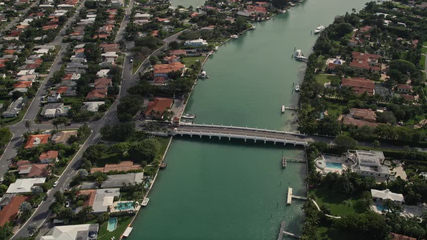 A drone view of a bridge connecting Indian Creek Village with Surfside in Florida spanning over a small waterway with residential areas and houses on both sides