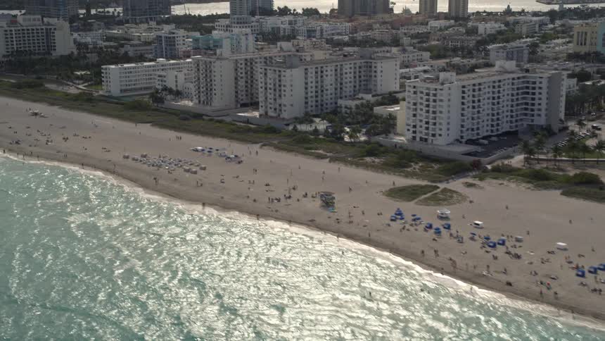 Aerial footage of a crowded South Beach Florida with buildings towering over the shoreline and people enjoying themselves on the beach