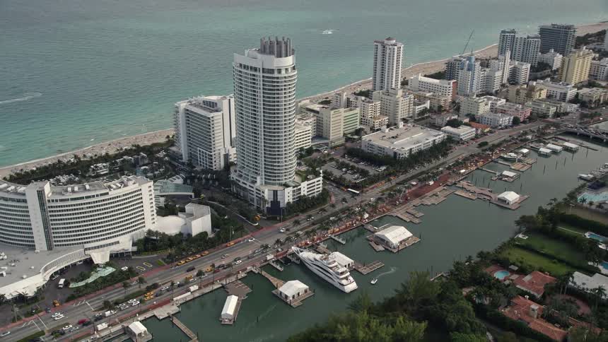 Aerial footage of a Miami Beach resort hotel and boardwalk during the day showcasing the coastline and approach towards the area