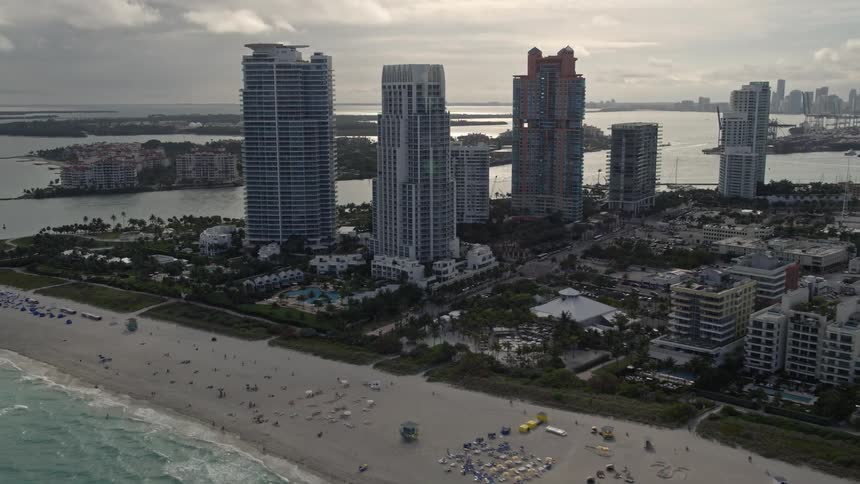 Orbiting aerial view of modern skyscrapers and beachgoers enjoying the coastline in South Beach Florida
